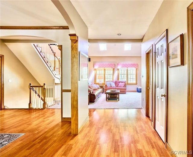 hall featuring light wood-style floors, arched walkways, baseboards, and stairway