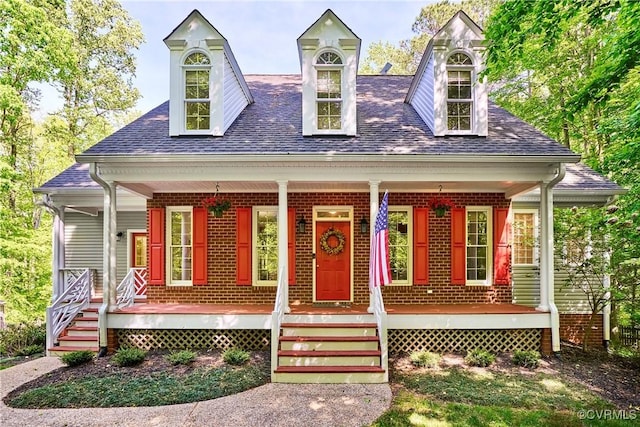 cape cod-style house with a porch, roof with shingles, and brick siding