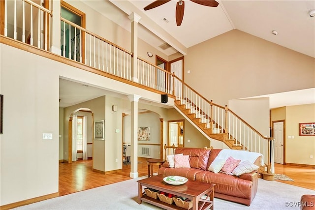 living area featuring ceiling fan, visible vents, arched walkways, stairway, and high vaulted ceiling