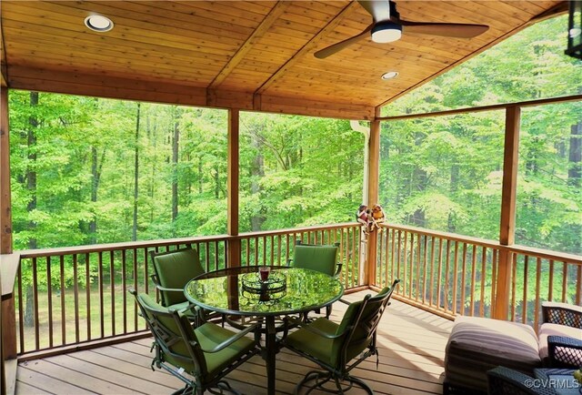 wooden terrace with a view of trees, a ceiling fan, and outdoor dining area
