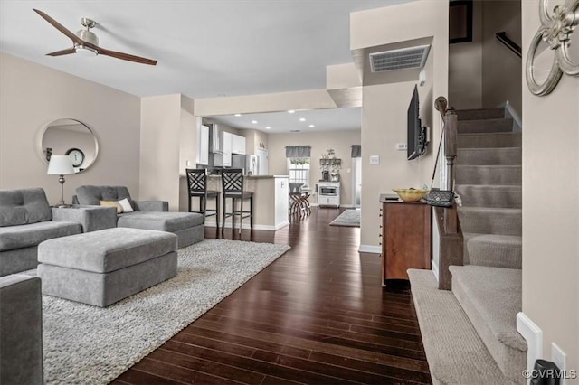 living area featuring ceiling fan, dark wood finished floors, stairs, baseboards, and visible vents
