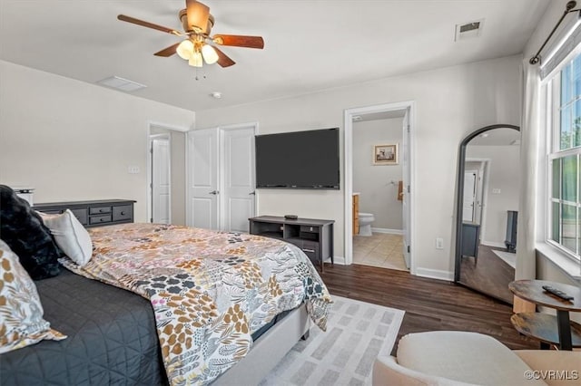 bedroom with ceiling fan, visible vents, wood finished floors, baseboards, and ensuite bathroom