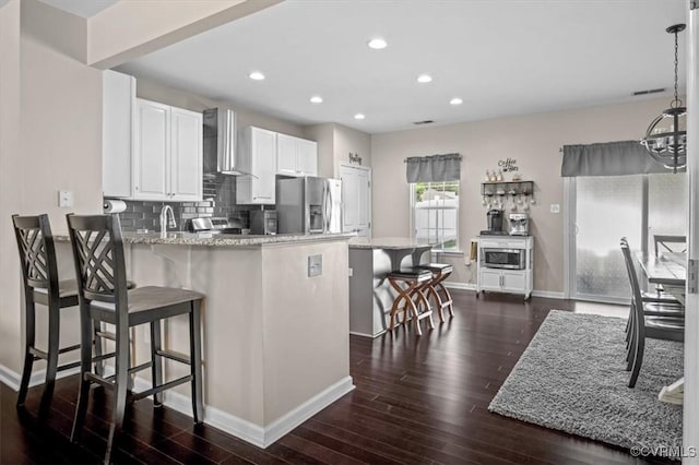 kitchen with wall chimney range hood, stainless steel fridge with ice dispenser, dark wood finished floors, baseboards, and a kitchen bar