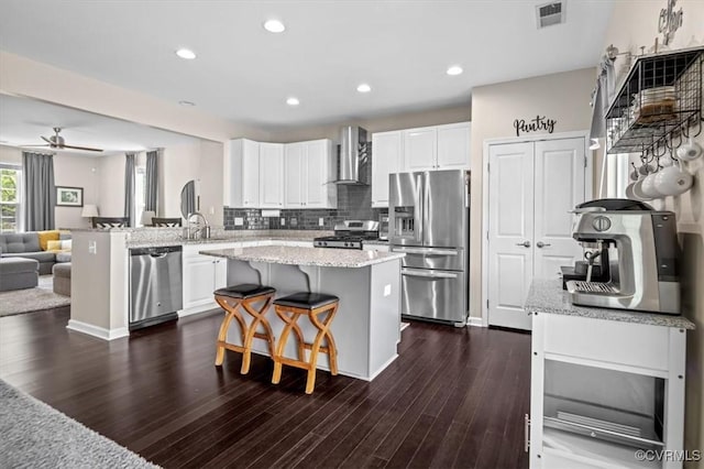 kitchen with white cabinets, appliances with stainless steel finishes, wall chimney exhaust hood, open floor plan, and visible vents