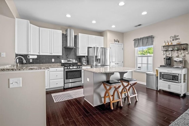 kitchen featuring visible vents, wall chimney range hood, a kitchen bar, white cabinets, and appliances with stainless steel finishes
