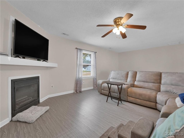 239 Marine Dr, Dunnsville, VA 22454 - living room with wood finished floors, a glass covered fireplace, ceiling fan, baseboards, and a textured ceiling