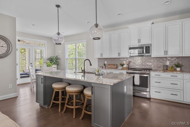 kitchen with light stone counters, appliances with stainless steel finishes, a kitchen island with sink, dark wood finished floors, and tasteful backsplash