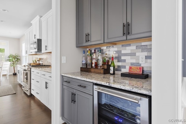 bar with backsplash, appliances with stainless steel finishes, a dry bar, dark wood-style floors, and wine cooler