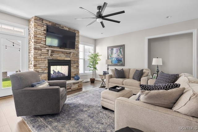 living room with a ceiling fan, baseboards, a stone fireplace, and wood finished floors