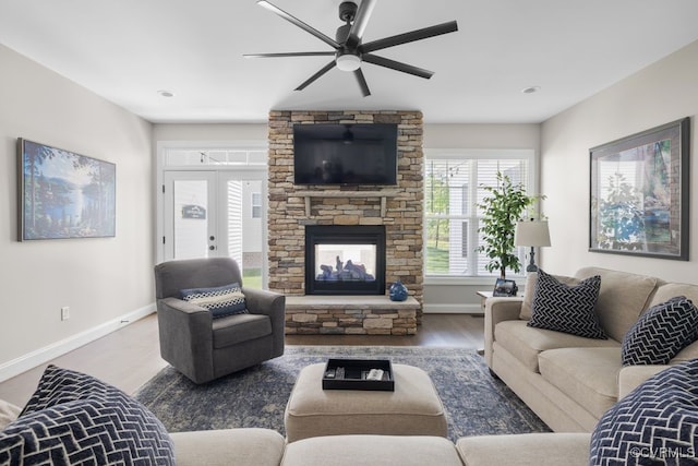 living area with a ceiling fan, baseboards, a stone fireplace, and wood finished floors