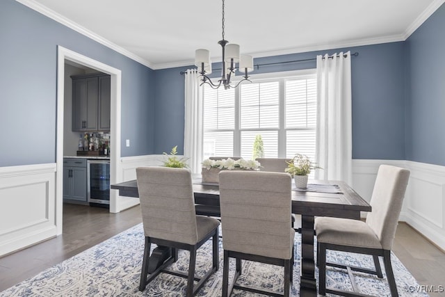 dining room with bar, a wainscoted wall, beverage cooler, an inviting chandelier, and ornamental molding