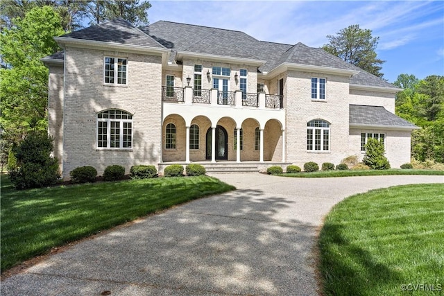 view of front of property with a balcony, a front yard, covered porch, brick siding, and driveway