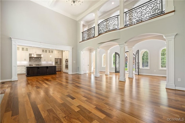 unfurnished living room with ornate columns, dark wood-style flooring, a towering ceiling, and baseboards