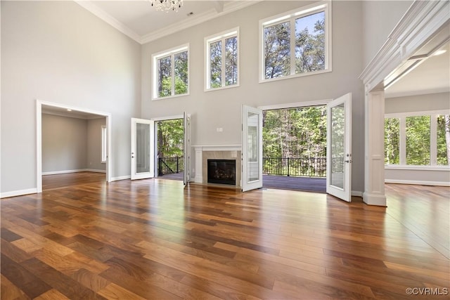 unfurnished living room featuring a towering ceiling, crown molding, hardwood / wood-style flooring, baseboards, and a glass covered fireplace