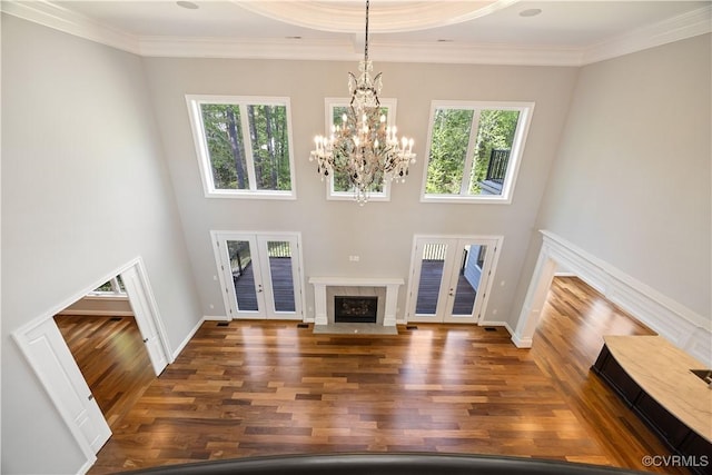 unfurnished living room featuring french doors, a fireplace with flush hearth, wood finished floors, an inviting chandelier, and ornamental molding