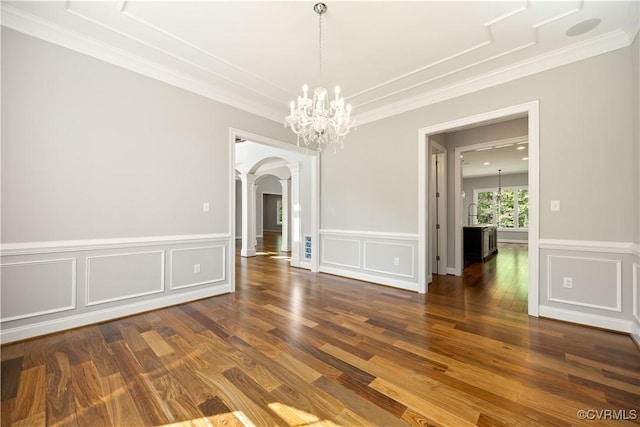 unfurnished dining area featuring wood finished floors, arched walkways, a decorative wall, and ornamental molding