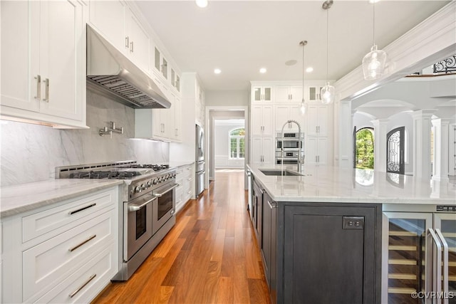 kitchen with decorative columns, wine cooler, under cabinet range hood, white cabinets, and appliances with stainless steel finishes