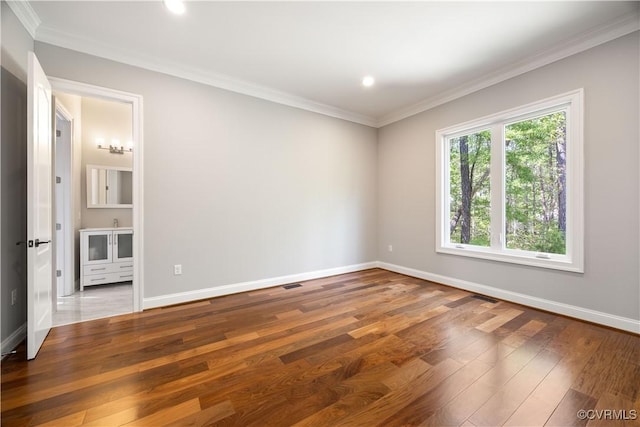 empty room featuring crown molding, baseboards, wood finished floors, and visible vents