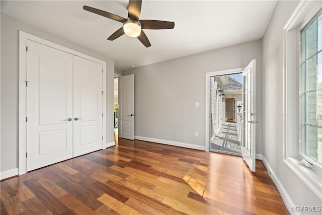 unfurnished bedroom with baseboards, multiple windows, wood finished floors, and access to exterior