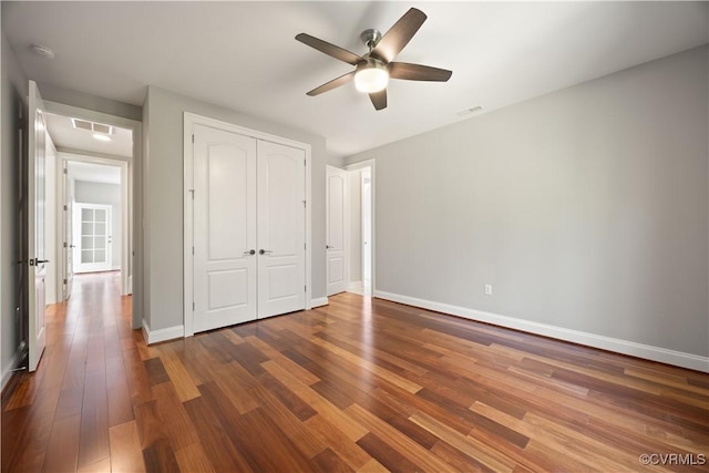 unfurnished bedroom featuring baseboards, a closet, wood finished floors, and visible vents