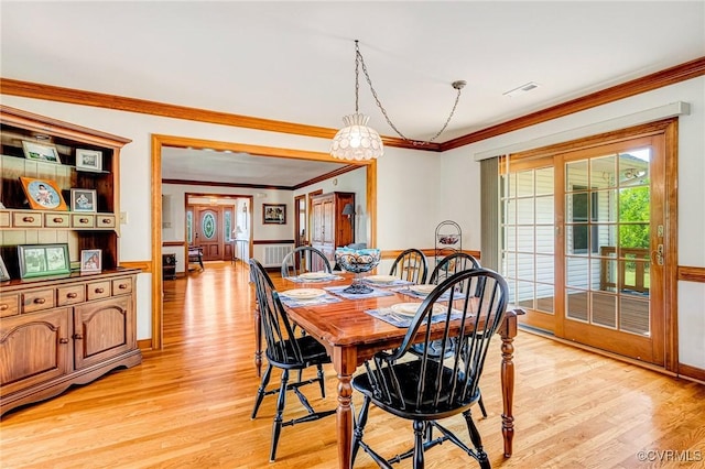 dining room featuring crown molding, light wood-style flooring, a wainscoted wall, and visible vents