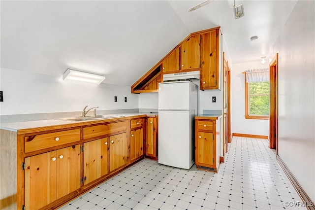 kitchen featuring brown cabinetry, a sink, freestanding refrigerator, lofted ceiling, and light floors