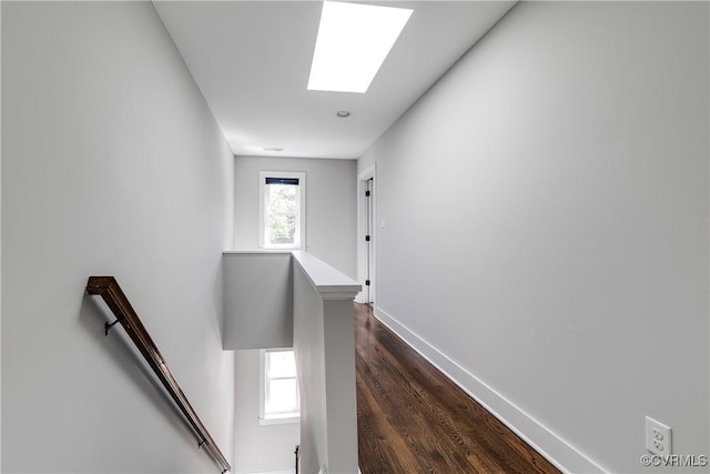corridor featuring baseboards, an upstairs landing, a skylight, and dark wood finished floors