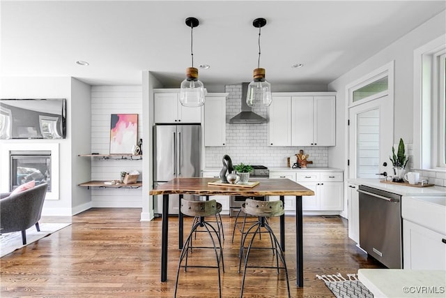 kitchen featuring wall chimney range hood, backsplash, appliances with stainless steel finishes, light countertops, and white cabinetry