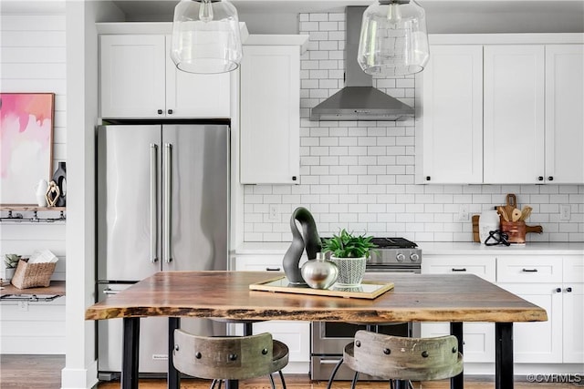 kitchen with high end refrigerator, white cabinetry, backsplash, and wall chimney range hood