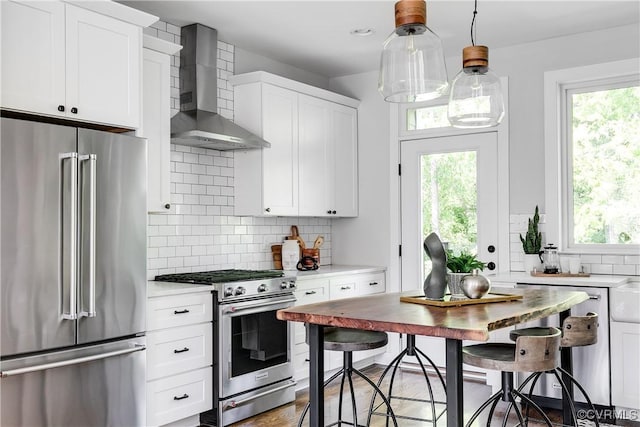 kitchen with high end appliances, a healthy amount of sunlight, wall chimney range hood, light countertops, and tasteful backsplash