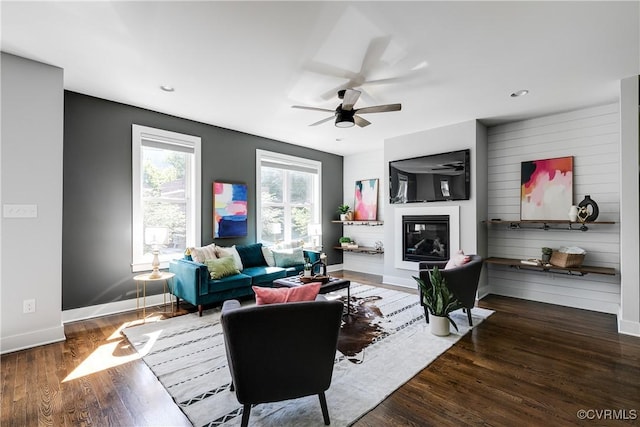 living room featuring a glass covered fireplace, a ceiling fan, baseboards, recessed lighting, and wood finished floors