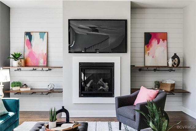 living area with a glass covered fireplace, baseboards, and wood finished floors