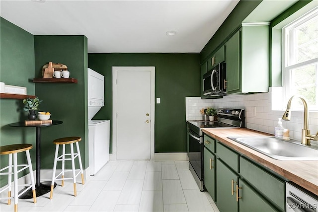 kitchen featuring stacked washer and dryer, tasteful backsplash, a sink, green cabinetry, and stainless steel appliances