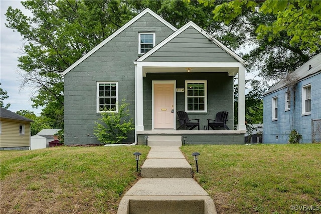 bungalow-style home with covered porch, concrete block siding, and a front yard