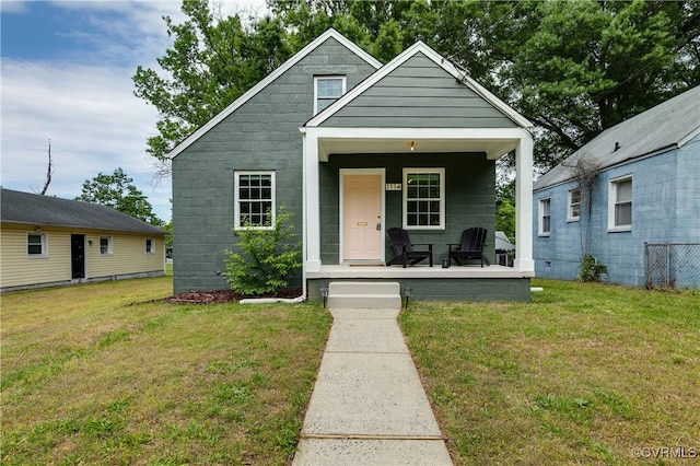 bungalow-style house featuring a front lawn, covered porch, and concrete block siding