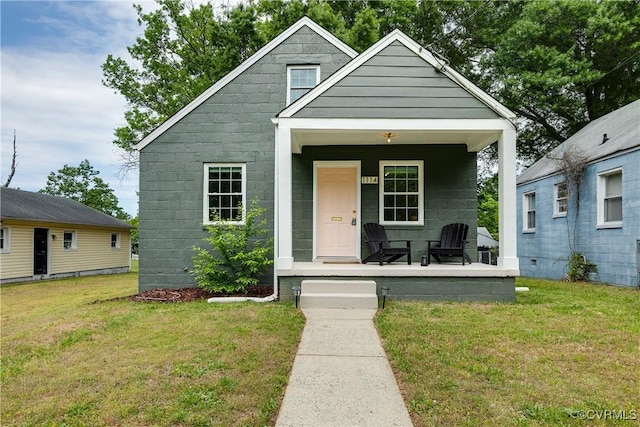 bungalow-style home with a porch, a front lawn, and concrete block siding