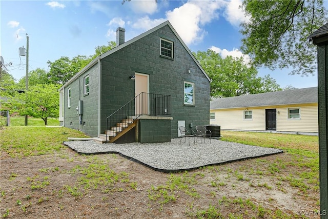 rear view of house featuring central air condition unit, a yard, a chimney, and concrete block siding