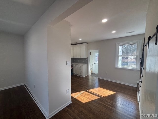 interior space featuring visible vents, a barn door, baseboards, and dark wood finished floors