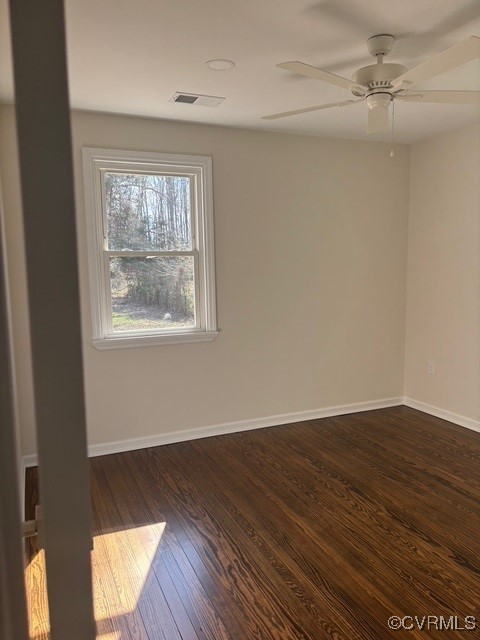 unfurnished room featuring visible vents, a ceiling fan, baseboards, and dark wood-style floors