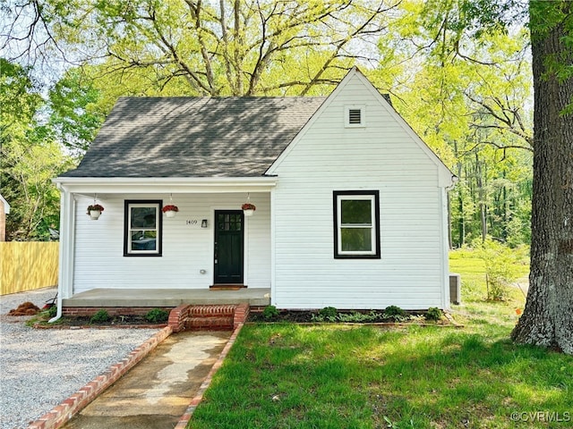 view of front facade with covered porch, fence, roof with shingles, and a front lawn