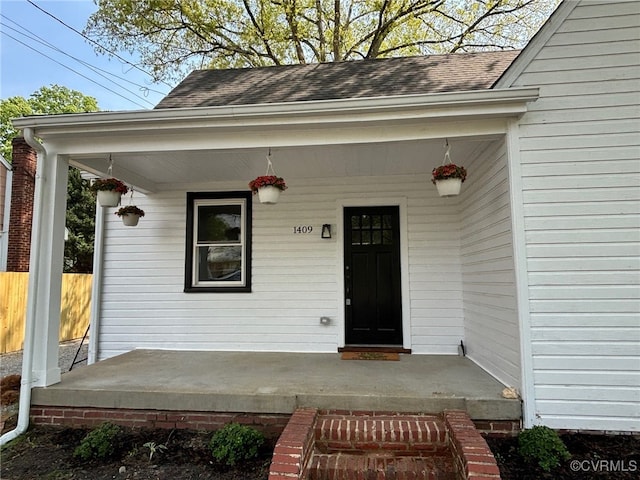 entrance to property with covered porch, fence, and roof with shingles