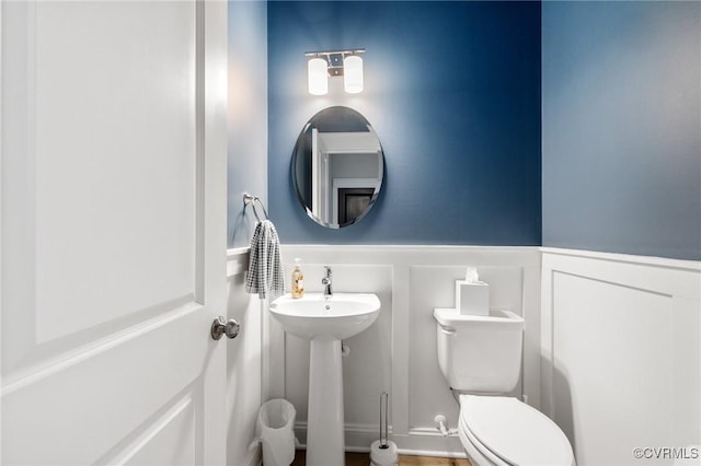 half bath with toilet, a sink, a wainscoted wall, and a decorative wall