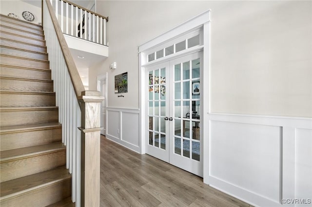 interior space with wood finished floors, a decorative wall, french doors, and a wainscoted wall