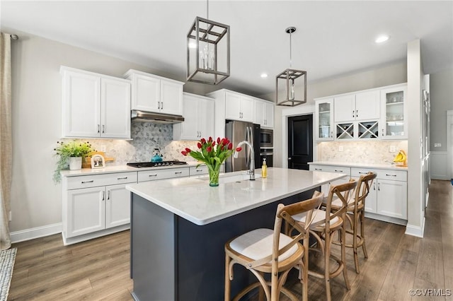 kitchen featuring dark wood-type flooring, light countertops, under cabinet range hood, appliances with stainless steel finishes, and backsplash