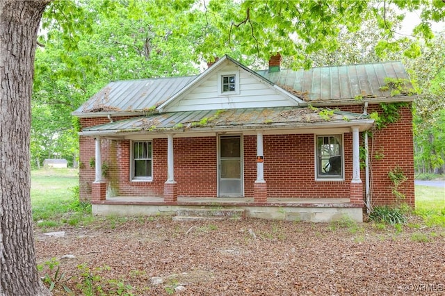 view of front of home with a standing seam roof, a chimney, a porch, and brick siding