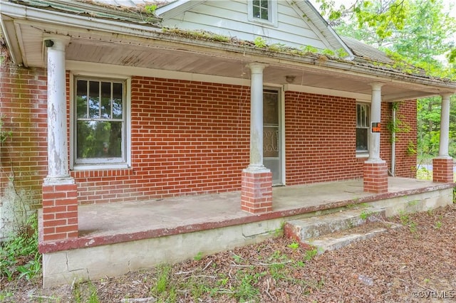 view of exterior entry featuring a porch and brick siding