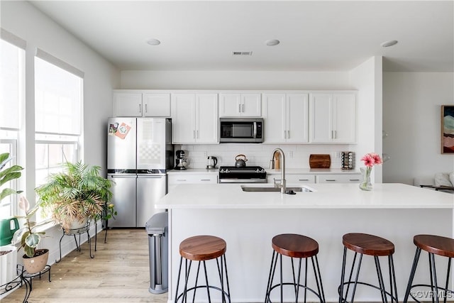 kitchen with visible vents, white cabinetry, a sink, backsplash, and stainless steel appliances