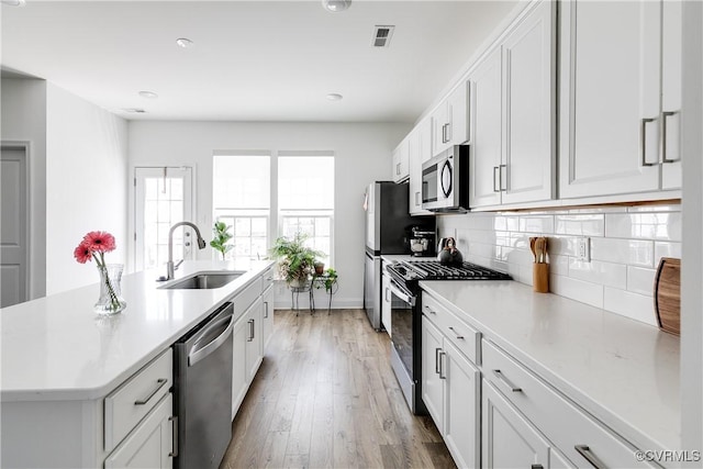 kitchen featuring a sink, a kitchen island with sink, light countertops, stainless steel appliances, and backsplash