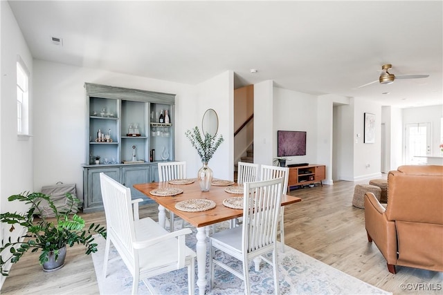 dining area featuring light wood-type flooring, a ceiling fan, stairs, and visible vents