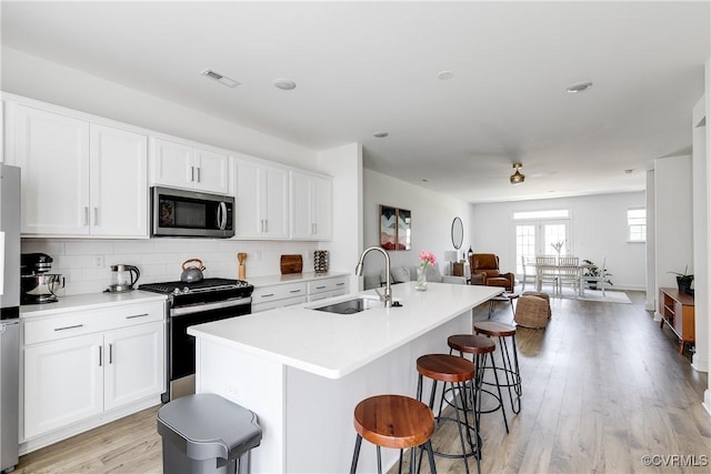 kitchen featuring visible vents, open floor plan, a sink, backsplash, and stainless steel appliances